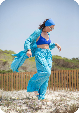 Romina, creadora de Indico Concept, posa llevando un pareo de playa azul claro, un bikini azul oscuro y una bandana y camisa azules.